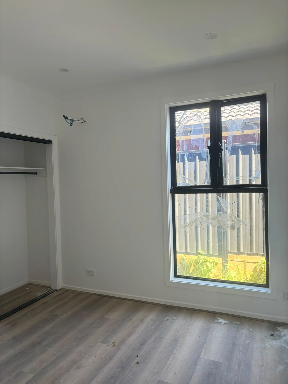 Light interior bedroom walls with a dark framed window and timber-look floor