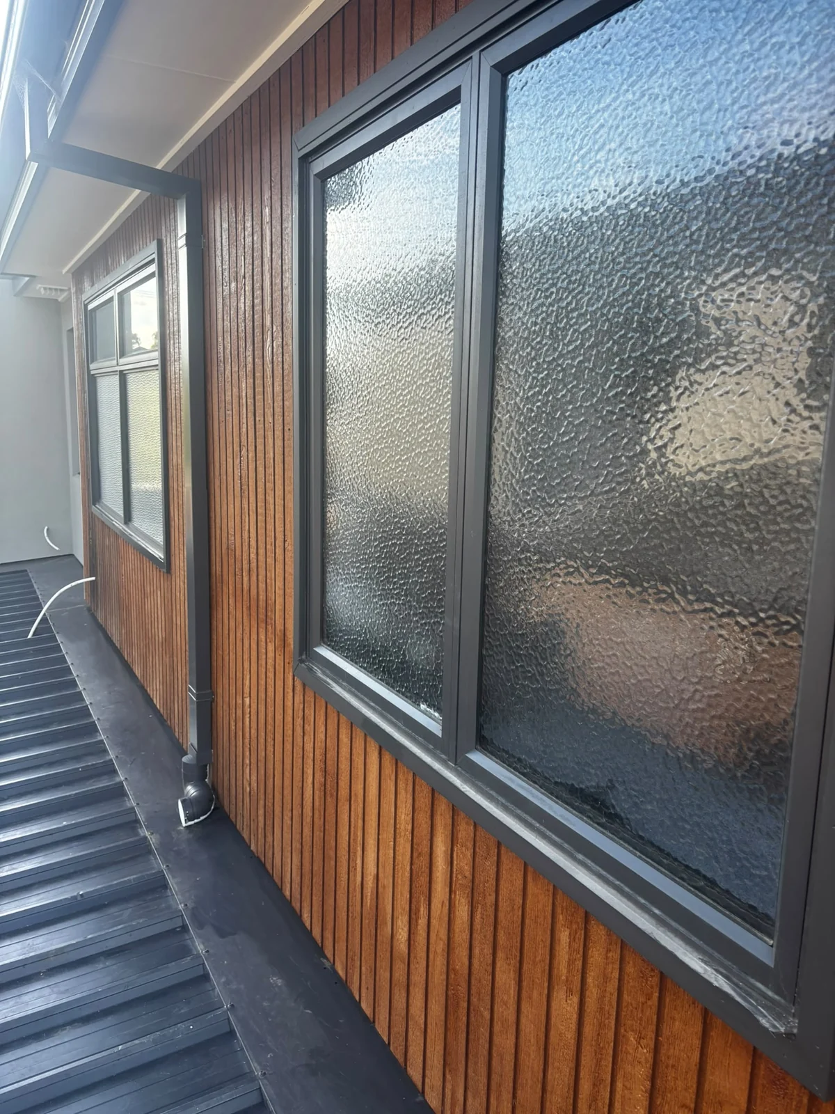 Timber-clad wall with dark framed textured-glass windows