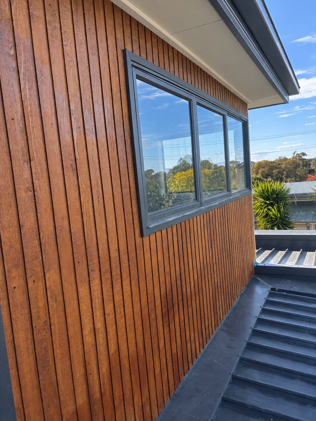 Exterior timber cladding around a dark framed window